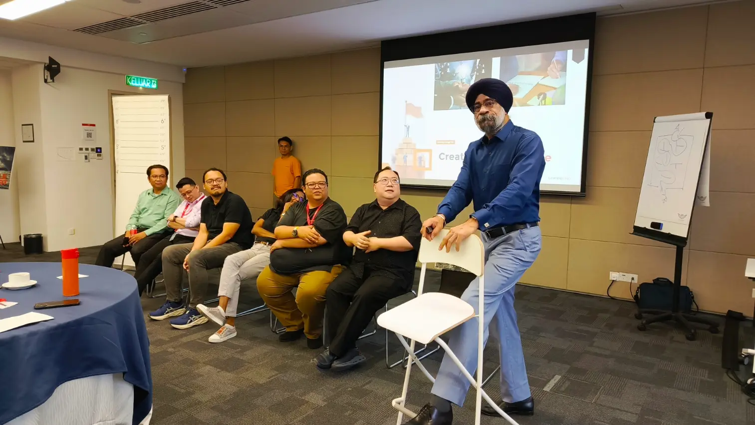 A Learning Edge facilitator standing on a chair to address a seated group during a leadership session